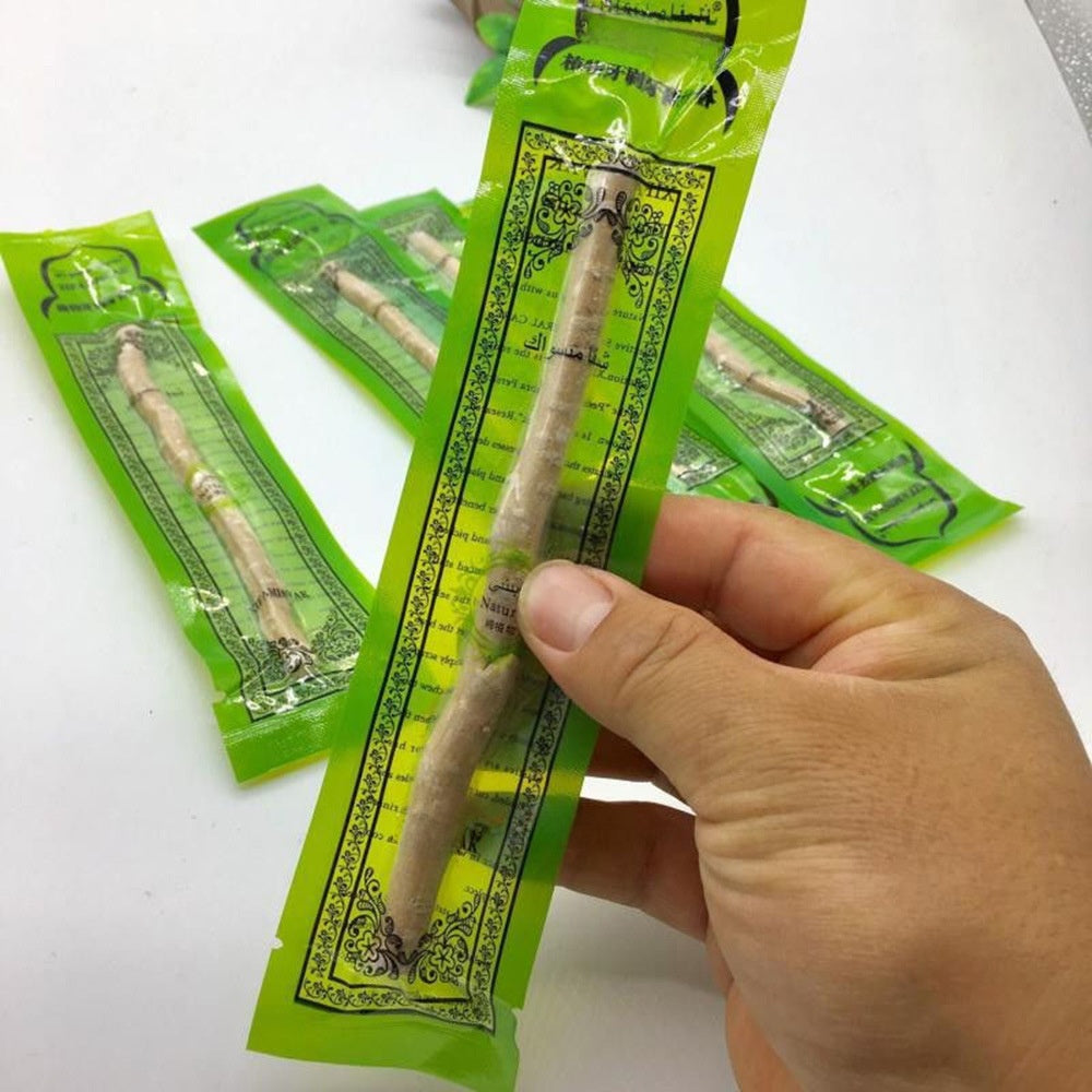 Hand holding a package of single miswak stick with green packaging on a white background
