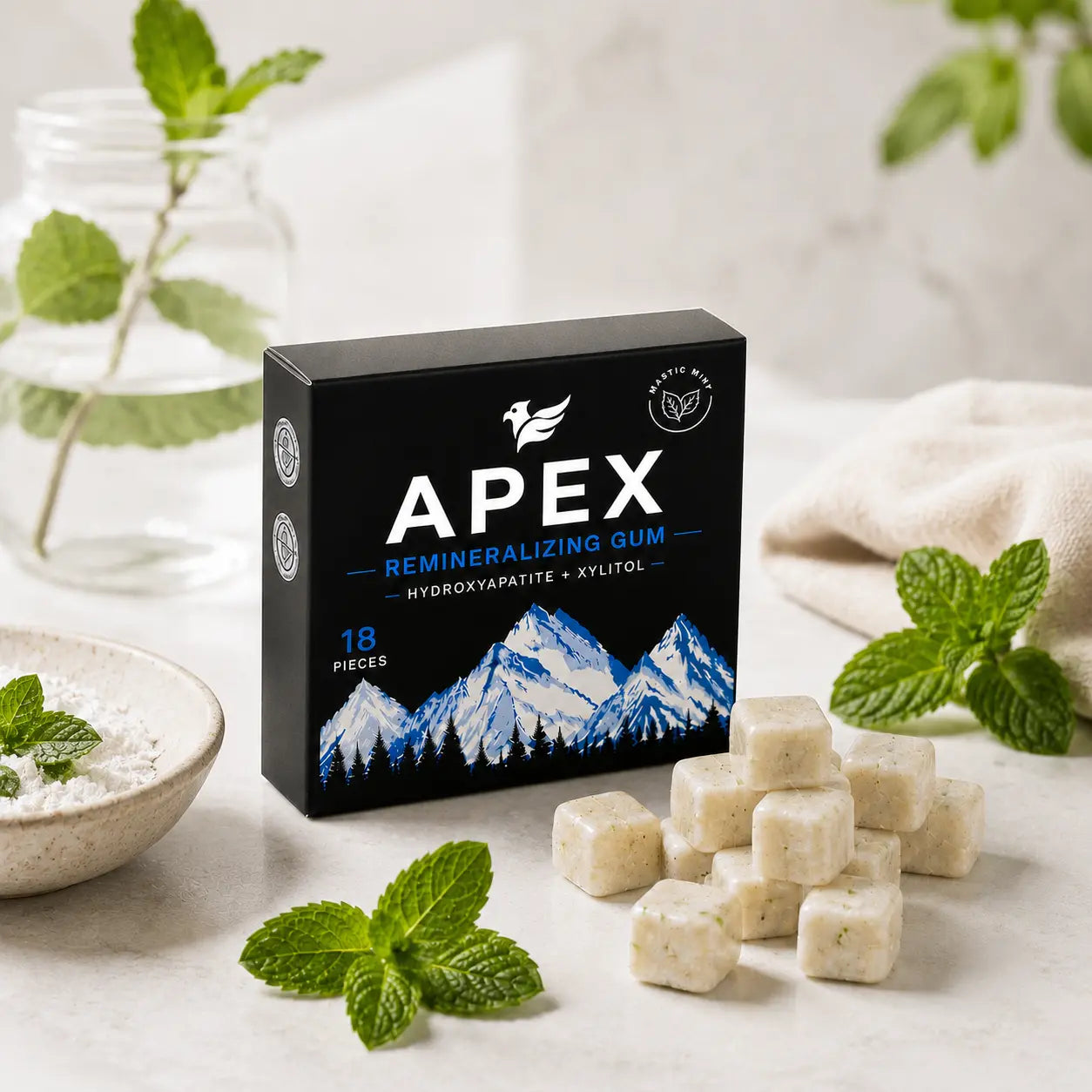 A box of APEX Remineralizing Gum chewable tablets sits on a light marble surface with mint leaves, a small bowl of powder, and a glass jar in the background.