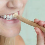 Person using a wooden miswak stick toothbrush to brush their teeth.